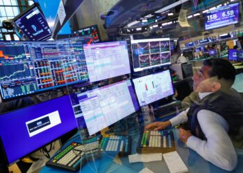 A stock trader sits at a desk surrounded by multiple monitors displaying complex charts, financial data, and trading software. The environment is busy, with other traders working in the background. The trading floor is filled with screens and financial information, the realm of future Stock Market Millionaires. | MAKE1M