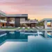 Modern luxury house with large windows and minimalist design, featuring spacious outdoor areas. The scene includes an expansive swimming pool, lounge chairs, and an outdoor screen, all set against a backdrop of a vibrant sunset and lush greenery. Ideal for those hiring a luxury real estate agent for millionaires. | MAKE1M