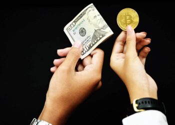 A pair of hands against a black background, one holding a roll of US dollar bills and the other holding a gold Bitcoin coin. The scene evokes the journey of a crypto millionaire, showcasing the contrast between traditional currency and digital cryptocurrency. | MAKE1M
