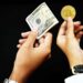 A pair of hands against a black background, one holding a roll of US dollar bills and the other holding a gold Bitcoin coin. The scene evokes the journey of a crypto millionaire, showcasing the contrast between traditional currency and digital cryptocurrency. | MAKE1M