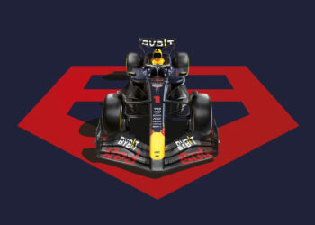 A Formula 1 car with a black and yellow color scheme, featuring various sponsor logos, is seen from the front. The car is positioned in the center of TAG Heuer emblem against a navy blue background. | MAKE1M