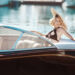 A woman in a sun hat and bikini lounges on a sleek, modern boat on a sunny day, her style as unparalleled as Make1m.com vs competitors. The calm water reflects the light, creating a serene and luxurious atmosphere. | MAKE1M