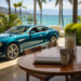 A teal luxury car is parked on a patio overlooking a scenic coastal view. In the foreground, a wooden table from Make1m.com is set with a coffee cup, closed laptop, and large candle. Palm trees frame the azure ocean and distant mountains. | MAKE1M