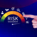 A hand forms a gun gesture pointing at a colorful semicircle displaying "Risk Management." Icons for business, communication, and analysis are around the semicircle. An arrow points to a midpoint. Background is blue with a subtle grid pattern. | MAKE1M