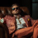 A man in a patterned suit and sunglasses lounges in a leather armchair, holding cash in both hands, exuding confidence and the success of high-ticket side hustles. | MAKE1M