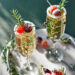 Two champagne glasses garnished with sugared cranberries and rosemary sprigs on a marble tray. Additional sugared cranberries and rosemary surround the glasses, creating a festive and elegant presentation. | MAKE1M