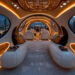 Futuristic luxury yacht interior with curved white seats, orange accent lighting, large windows showing a city skyline at dusk, and high-tech controls at the front. | MAKE1M