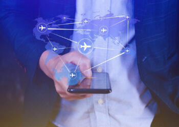 A person holding a smartphone with a digital overlay of a world map and airplane icons connected by lines, symbolizing global travel or online flight booking. | MAKE1M